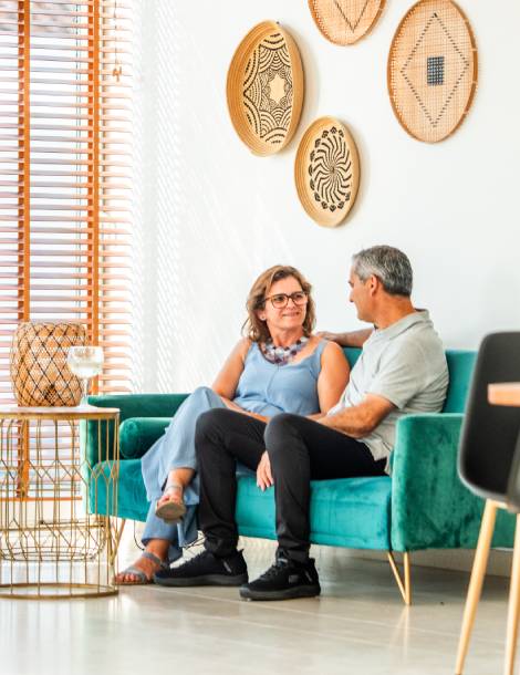 Pareja sentada en un sofá verde, conversando junto a una mesa con bebida.