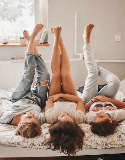 Tres personas acostadas en una cama con las piernas levantadas hacia arriba.