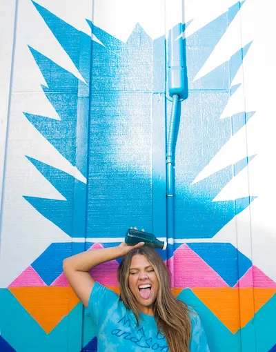 Mujer alegre con camiseta azul, posa con grafiti colorido de fondo.