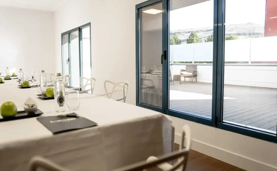 Sala de reuniones con mesa, sillas y grandes ventanales con vista al exterior.