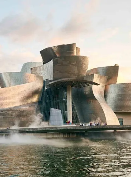 Edificio moderno con fachada metálica ondulante junto a un río.