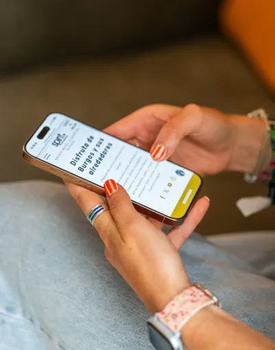 Persona sosteniendo un teléfono con una página web abierta. Uñas pintadas de naranja y reloj rosa.