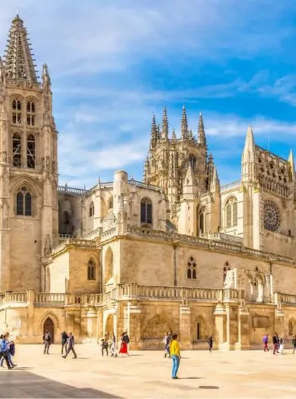 Catedral gótica con personas caminando frente a ella bajo un cielo azul.