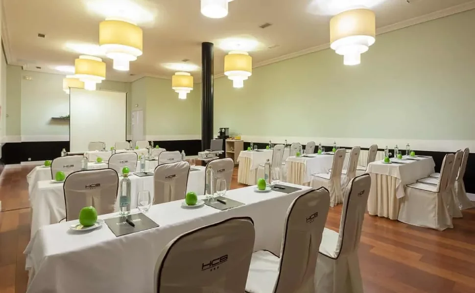 Sala de conferencias con mesas, sillas blancas y luces de techo.