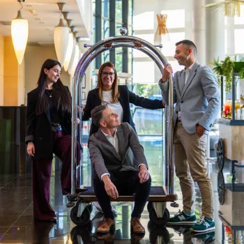Cuatro personas con ropa elegante junto a un carrito de hotel en un vestíbulo moderno.
