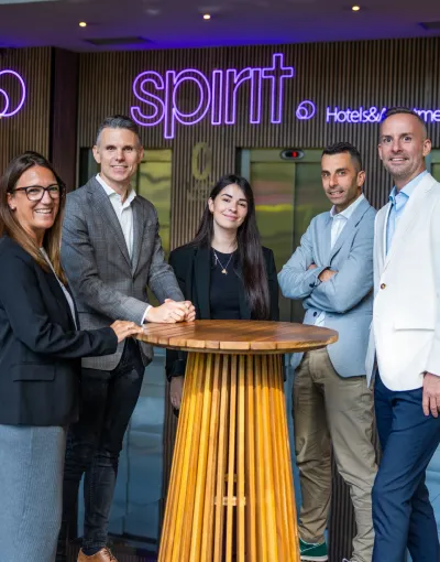 Cinco personas posan junto a un mostrador de madera frente a un letrero que dice "spirit".