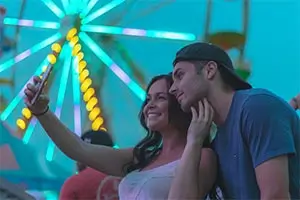 Pareja tomándose una selfie frente a una rueda de la fortuna iluminada.