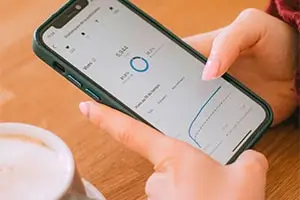 Persona revisa estadísticas en su celular junto a una taza de café.