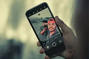 Persona tomando una selfie con otra persona en el fondo.