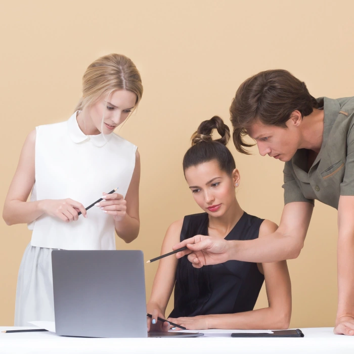 Tres personas trabajan juntas frente a una laptop, colaborando y señalando la pantalla en una oficina.