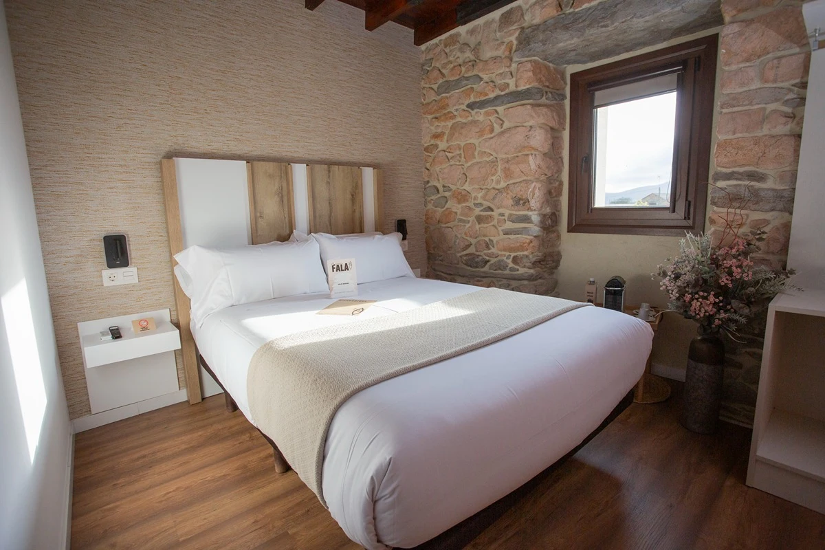 Cuarto con cama de matrimonio y pared de piedra con ventana.