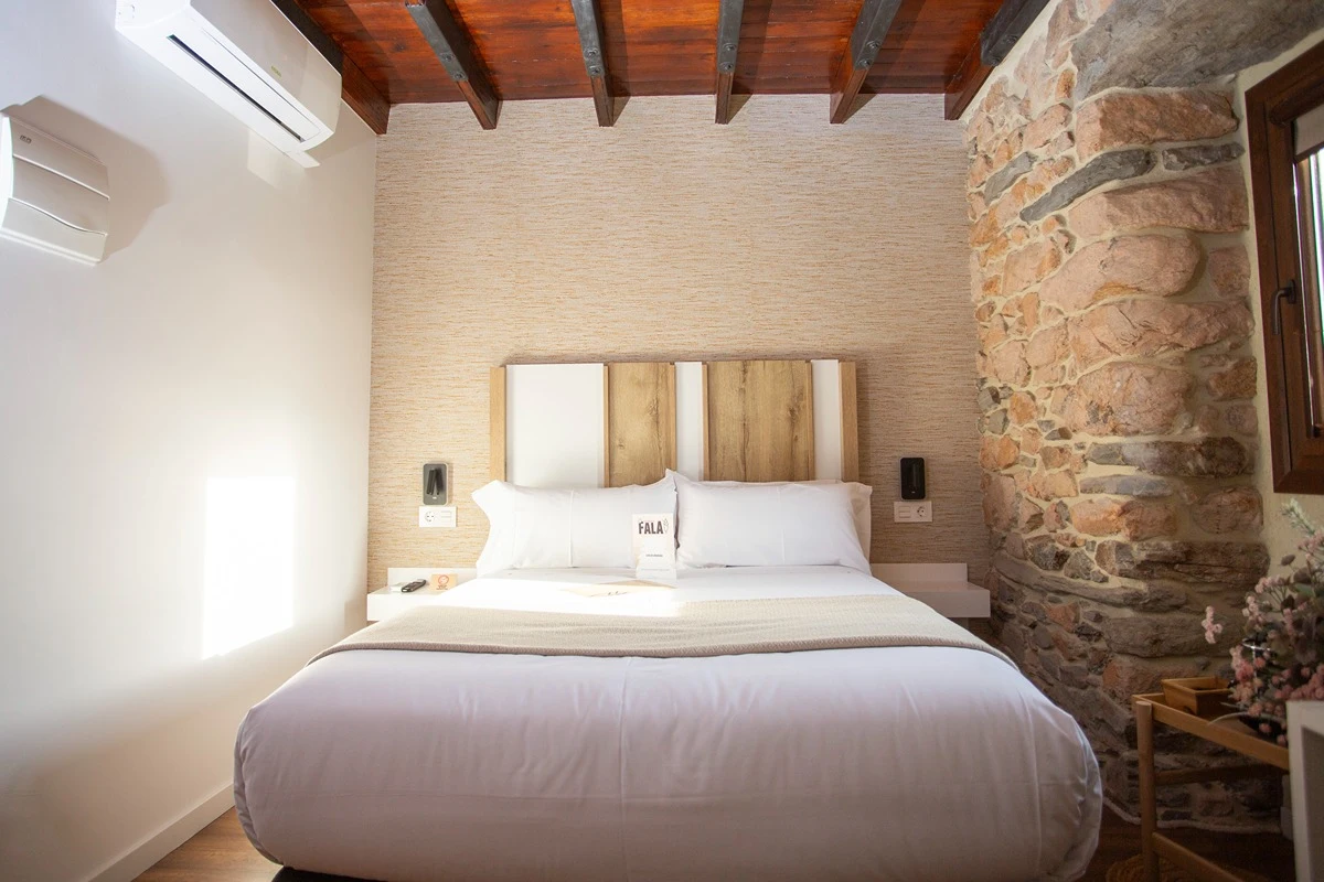 Cuarto con cama de matrimonio y pared de piedra con ventana t techo de madera.