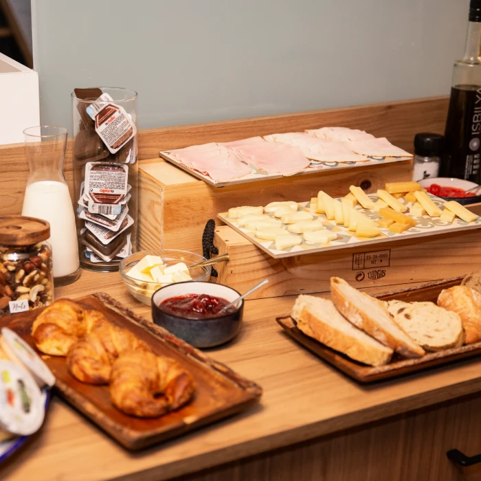 Mesa de desayuno con pan, croissants, quesos, embutidos y leche.