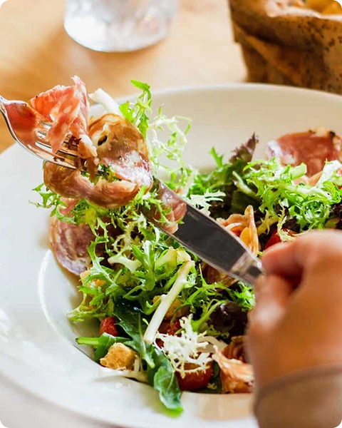 Ensalada con jamón y lechuga en un plato blanco, tenedor y cuchillo en uso.