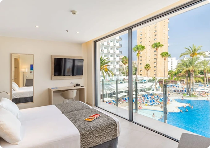 Habitación de hotel moderna con vista a la piscina y edificios, decorada en tonos claros.