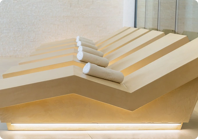 Camillas inclinadas en spa, con toallas enrolladas sobre cada una, en un ambiente moderno y cálido.