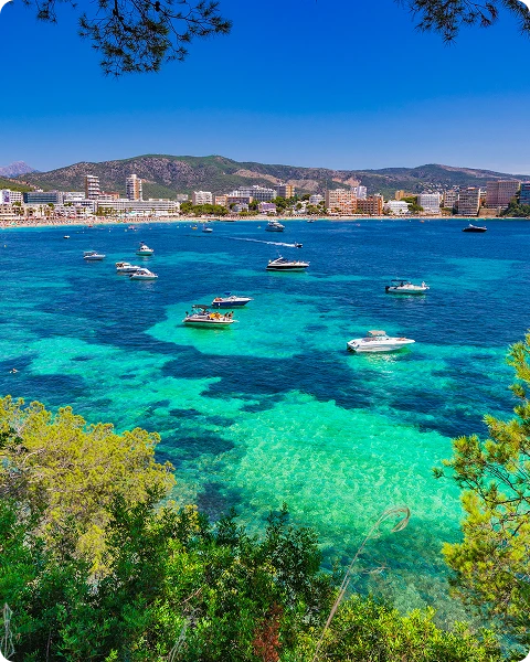 Bahía con aguas turquesas y barcos; ciudad y montañas al fondo bajo un cielo azul claro.