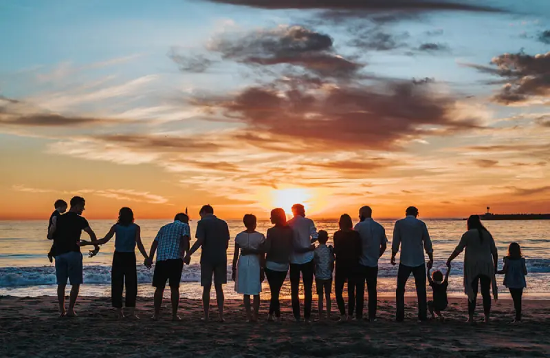 Grupo de personas de espaldas, tomados de la mano, mirando el atardecer en la playa.