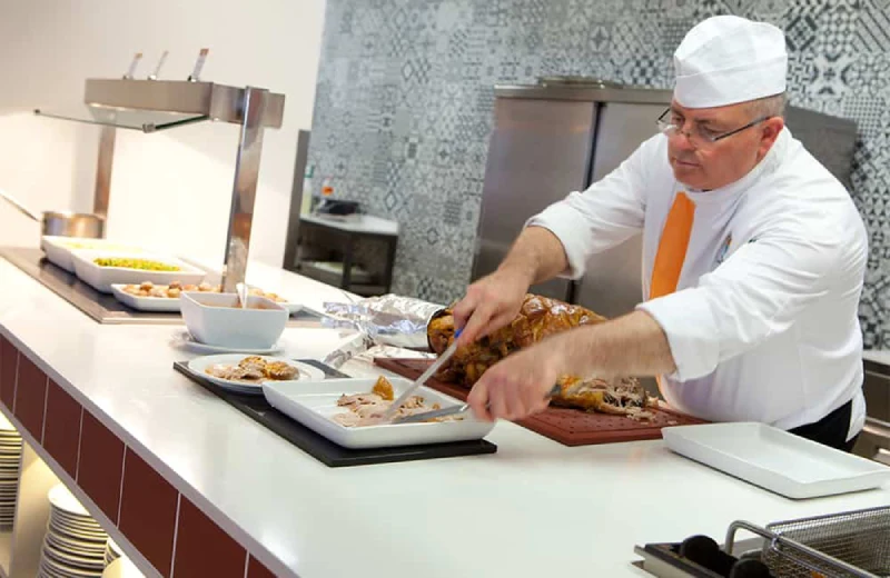 Chef cortando carne en una cocina con platos y bandejas a su alrededor.