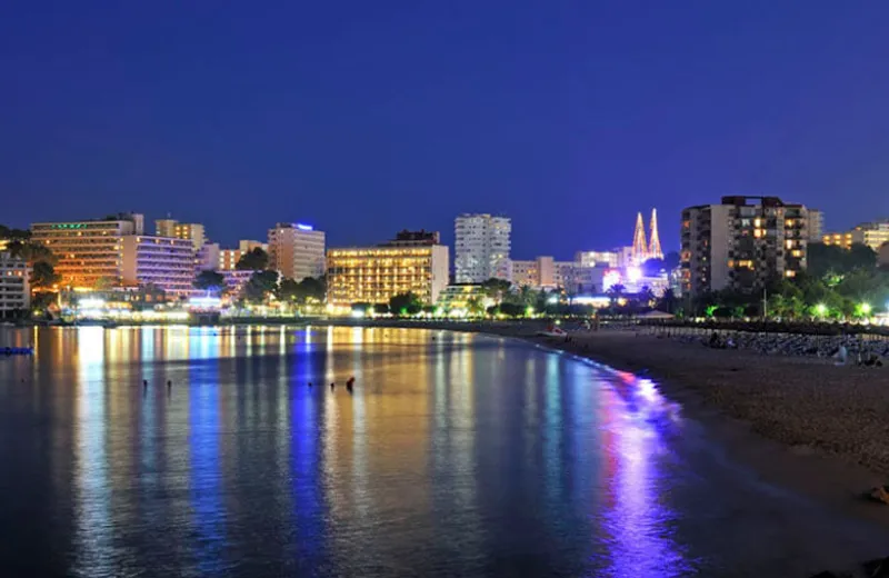 Vista nocturna de la ciudad con luces reflejadas en el agua y edificios iluminados.