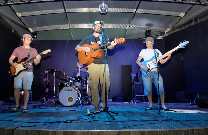 Banda tocando en vivo en un escenario al aire libre, con guitarras, bajo y batería.