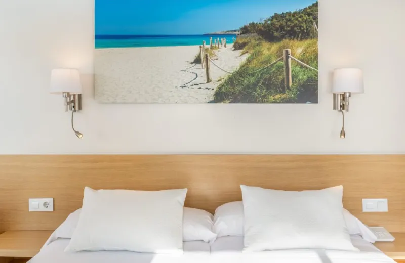 Habitación con cama, cuadro de playa y lámparas de pared a los lados.