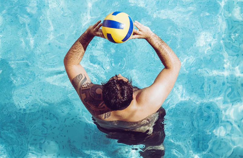 Hombre con tatuaje juega con una pelota en una piscina.