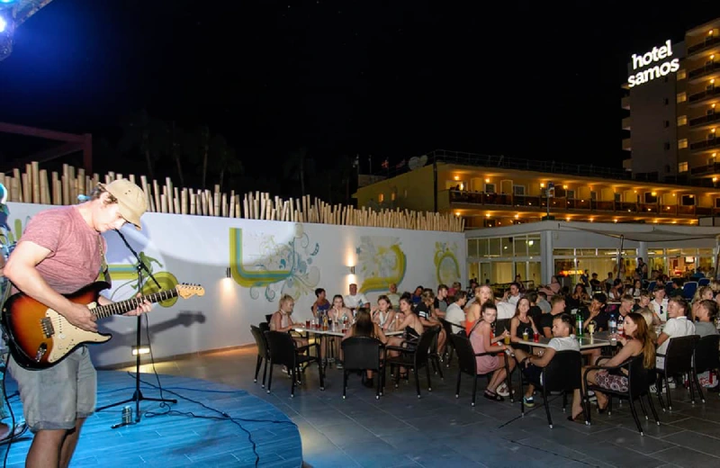 Un músico toca guitarra en vivo frente a una audiencia en un lugar al aire libre, de noche.