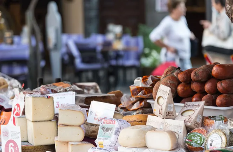 Mesa con variedad de quesos y embutidos en un mercado al aire libre.