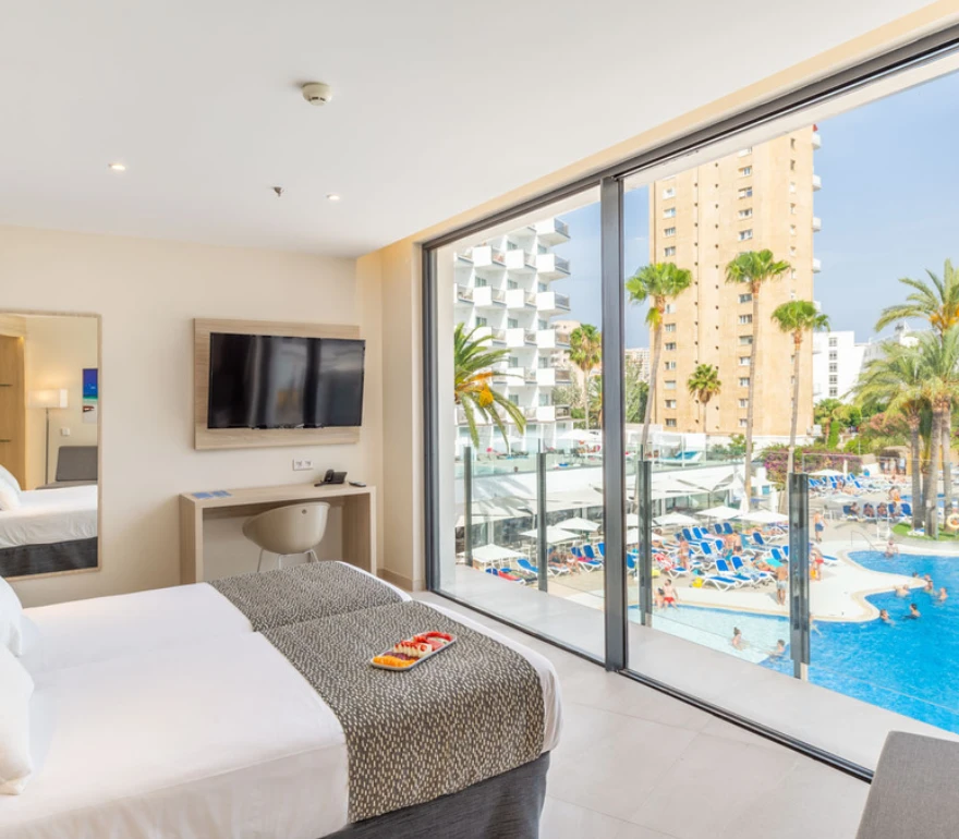 Habitación de hotel moderna con vista a una piscina exterior y edificios altos rodeados de palmeras.