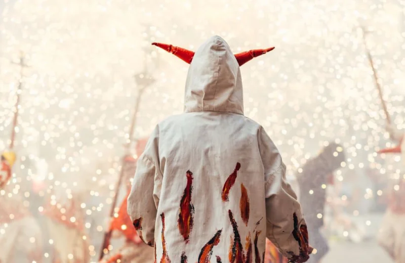 Persona disfrazada con capa y cuernos rojos en una fiesta con chispas alrededor.