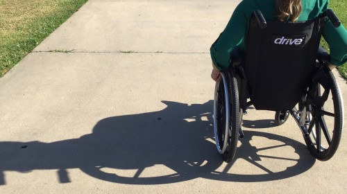 Persona en silla de ruedas en camino de cemento, con sombra proyectada.