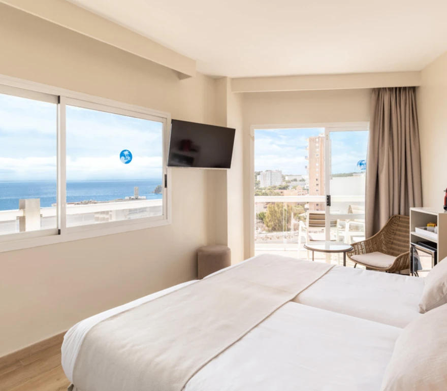 Habitación luminosa con cama doble, televisor, balcón y vista al mar.