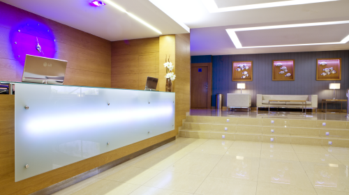 Recepción moderna con mostrador iluminado, paredes de madera y sillones blancos al fondo.