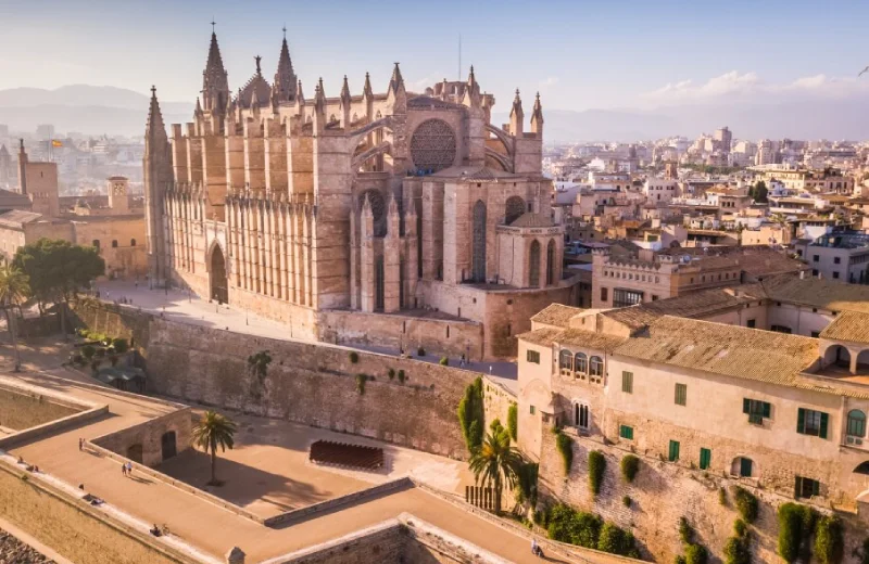 Catedral gótica en una ciudad con murallas y paisaje urbano al fondo.