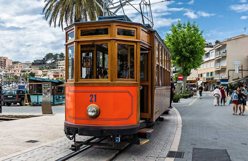Tranvía clásico naranja circulando por una calle en un área urbana con palmeras y edificios.