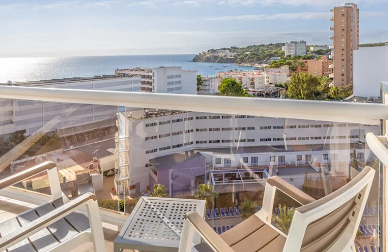 Vista desde un balcón con sillas, edificios al fondo y el mar en el horizonte.