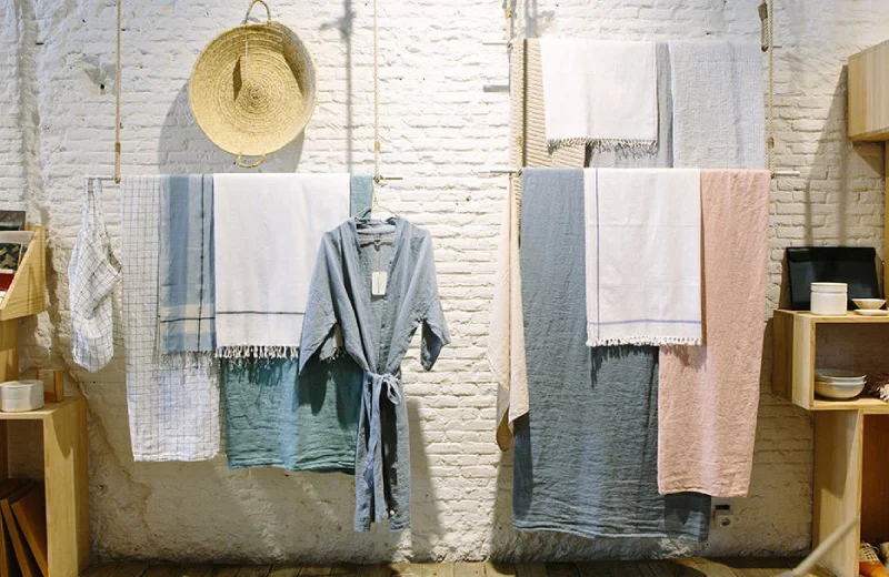 Ropa y toallas colgadas en una pared de ladrillo, junto a un sombrero de paja decorativo.