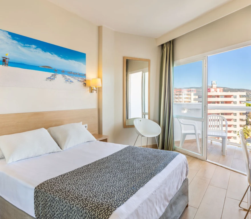 Habitación de hotel luminosa con cama doble, balcón y una gran pintura de playa en la pared.