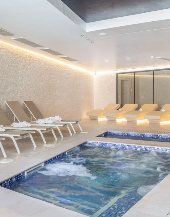 Sala de spa con jacuzzi, tumbonas y luces ambientales cálidas en un entorno moderno.