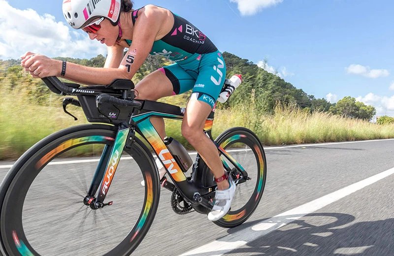 Ciclista con casco compite en carretera, montando bicicleta de colores vivos bajo un cielo azul.