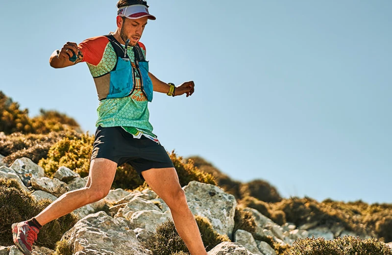 Corredor en ropa de senderismo desciende por un sendero rocoso en una montaña.