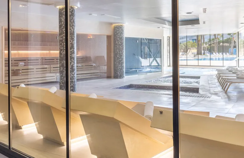 Spa moderno con piscina, sillas reclinables, luz natural y ambiente sereno.