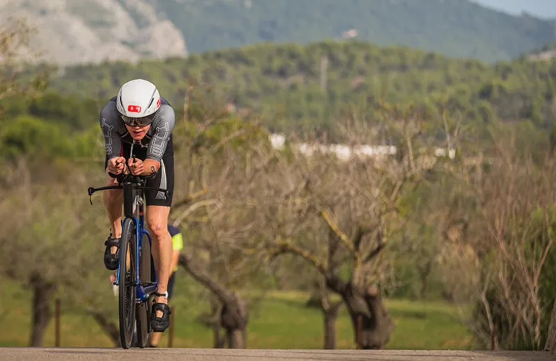 Ciclista en traje aerodinámico y casco, compite en un paisaje montañoso.