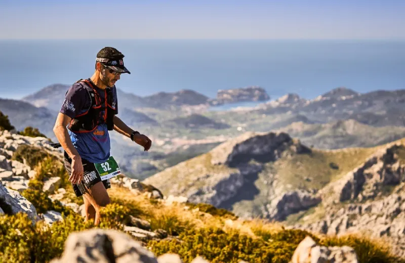 Corredor en montaña con vista al mar, cielo despejado y paisaje rocoso.