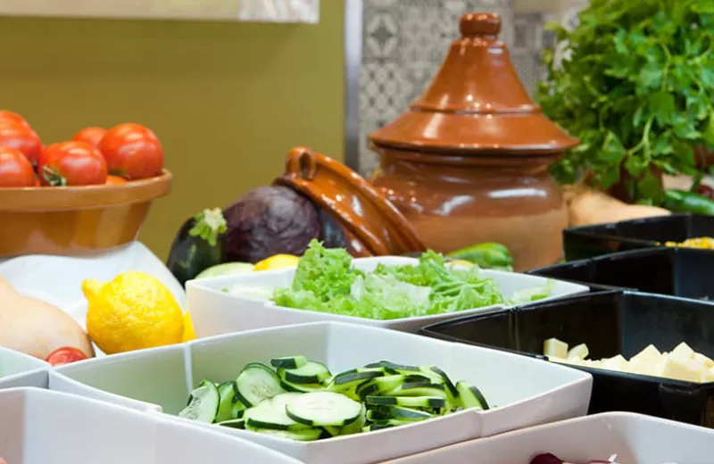 Verduras frescas en platos y tomates cerca de una olla de barro decorativa.