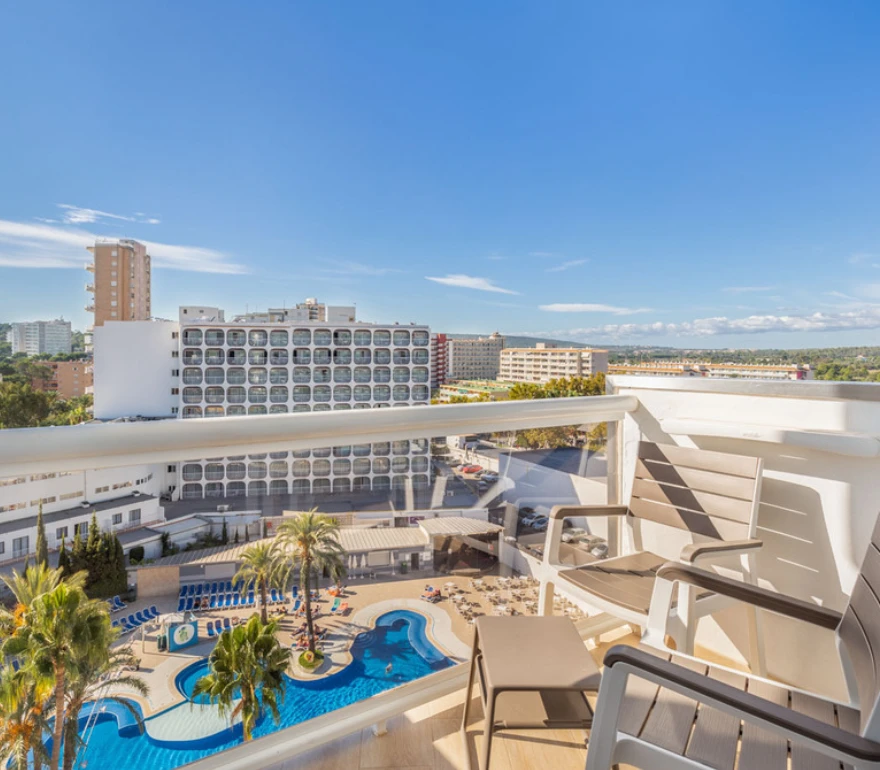 Vista desde un balcón con sillas, piscina y edificios al fondo bajo un cielo despejado.