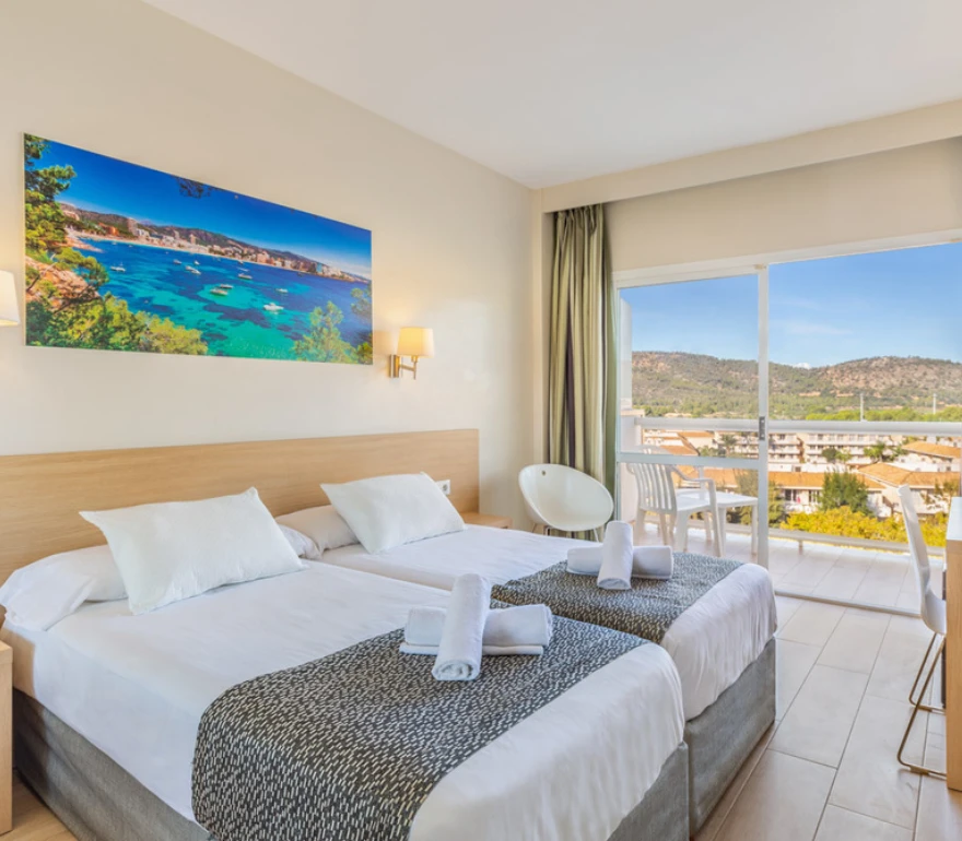 Habitación de hotel luminosa con dos camas individuales y vista panorámica desde una ventana amplia.