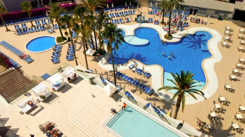 Vista aérea de un complejo con varias piscinas, sillas de playa y palmeras.