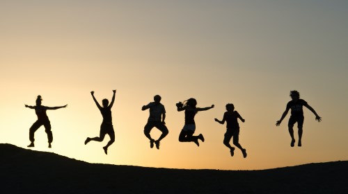 Personas saltando en el aire al atardecer, capturadas en silueta sobre una colina.